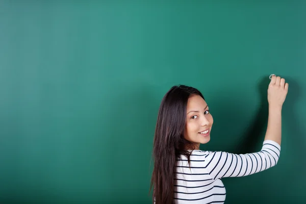 Smiling student writing on empty blackboard