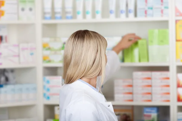 Female pharmacist taking medicine from shelf