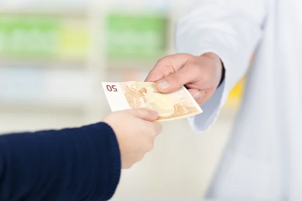 Customer's Hand Passing Money To Male Pharmacist In Pharmacy