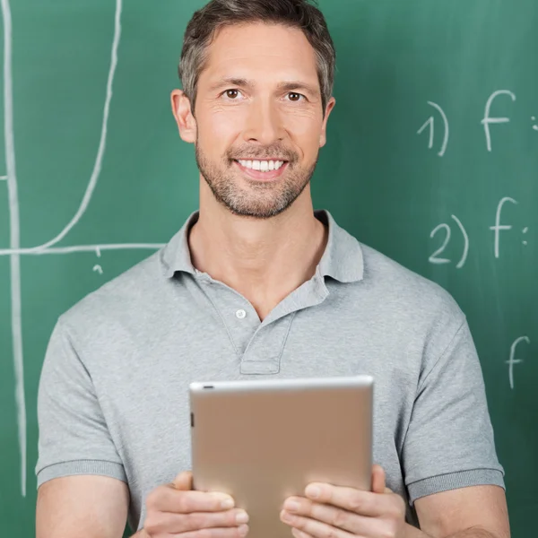Male Teacher Holding Digital Tablet Against Chalkboard