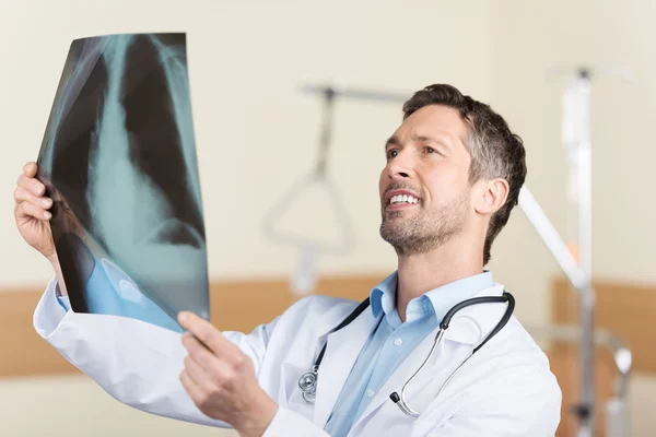 Mature Doctor Looking At X-Ray Report In Hospital