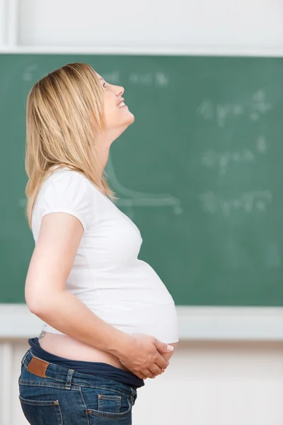 Pregnant Teacher With Hands On Belly Standing In Classroom