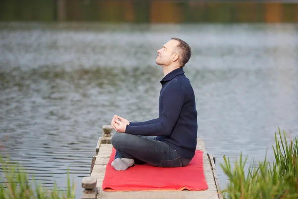Man Meditating In Lotus Position On Pier Against Lake