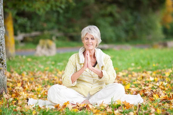 Senior Woman With Hands Clasped Meditating In Park