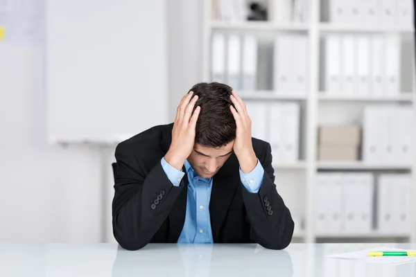 Stressed Businessman With Head In Hands At Desk