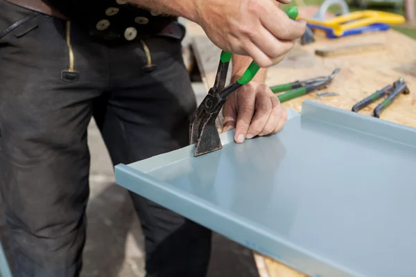 Roofer folding a metal sheet using special pliers