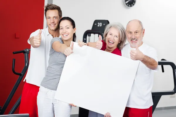 Family With Blank Billboard Gesturing Thumbs Up In Gym