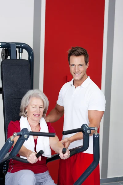 Trainer Assisting Senior Woman Using Rowing Machine