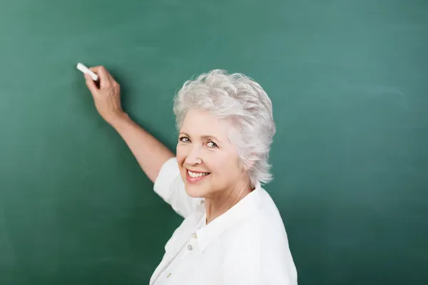 Senior woman writing on a chalkboard — Stock Photo #30761559