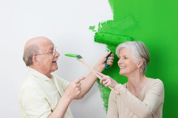 Playful senior couple painting their house green