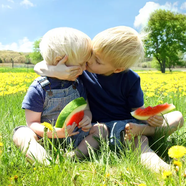 Young Children HUgging as they Eat Fruit Outside