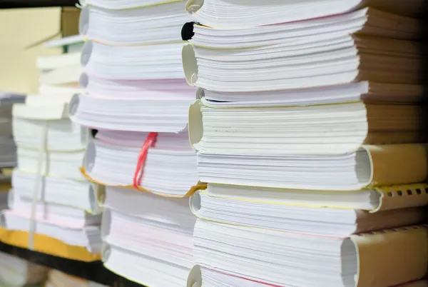 Pile of documents on desk stack up high waiting to be managed.