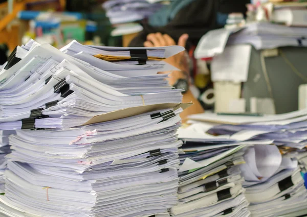 Pile of documents on desk stack up high waiting to be managed.