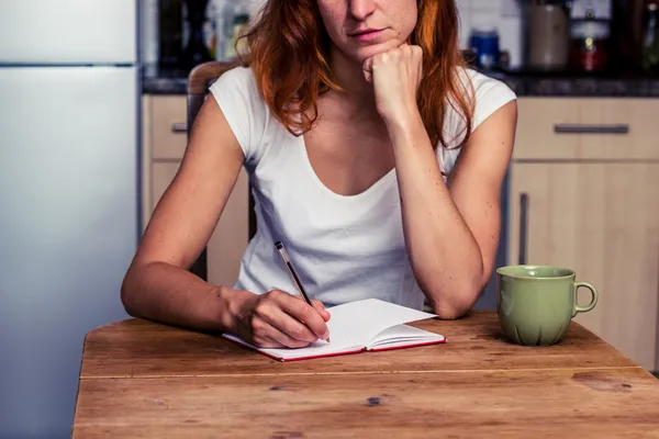 Woman making a shopping list in her kitchen