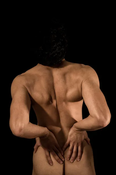 Young man with lower back pain, naked on black background