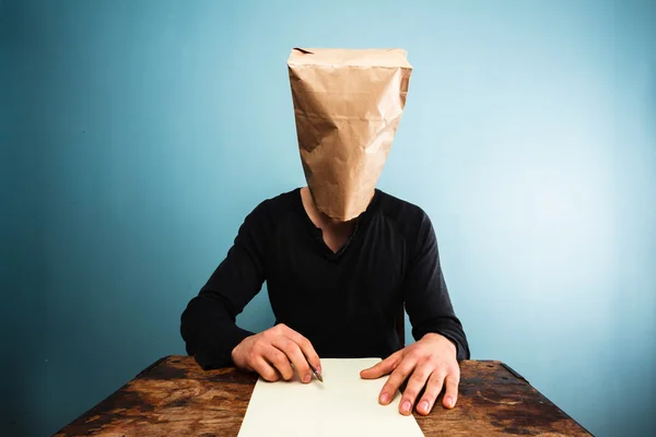 Man with bag over head writing letter