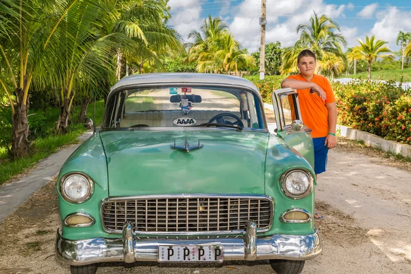 Young adolescent standing beside his vintage retro classic car