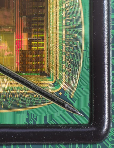 Open computer chip with gold wire connections compared to a needle