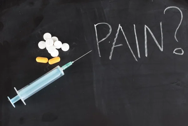 Syringe and pills on chalkboard with pain