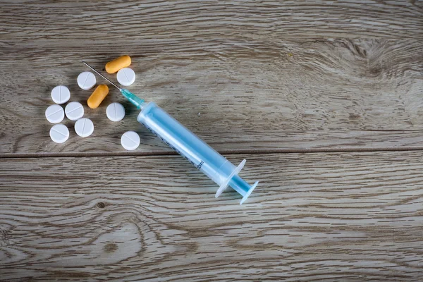Syringe and pills on wooden board