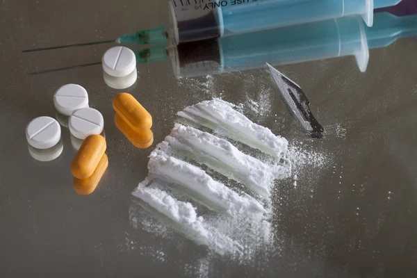 Syringe, pills, blade and depiction of cocaine on mirror