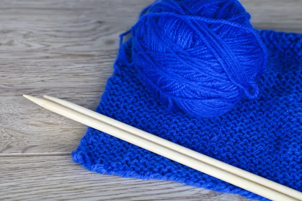 Skein of blue knitting yarn with bamboo needles and completed knitting