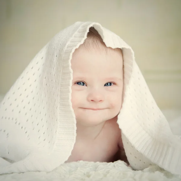 Little baby with Down syndrome hid under blanket and smiles slyly