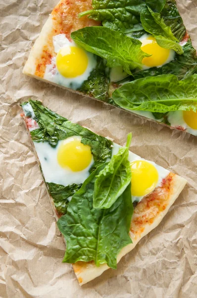 Two pieces of pizza with quail eggs and spinach