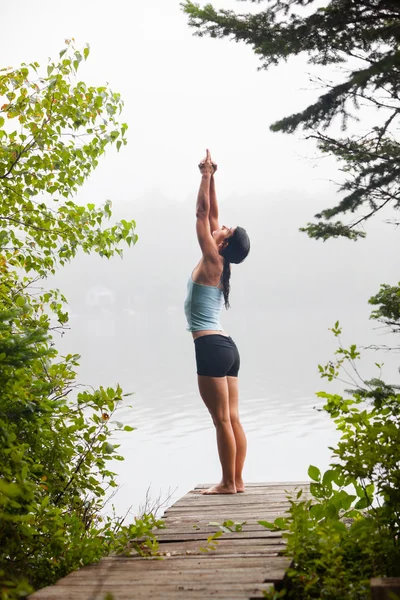 Woman doing yoga on dock by lake