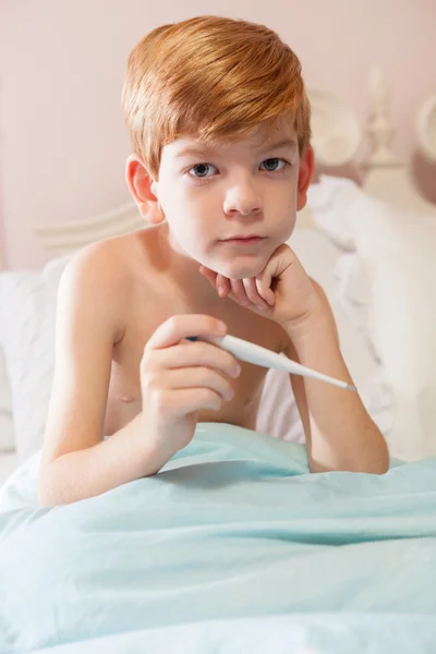 Boy sitting in bed with thermometer.