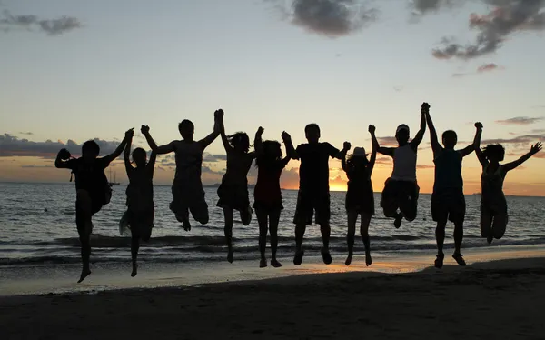 Silhouette of friends jumping on beach during sunset time