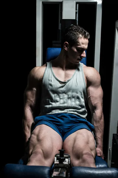 Bodybuilder doing heavy weight exercise for legs on machine leg extensions