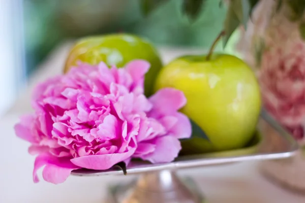 Green apples and beautiful peony flowers on table. Sunny day