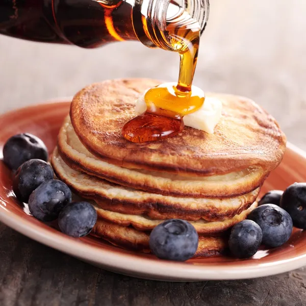 Pouring maple syrup on stack of pancakes.