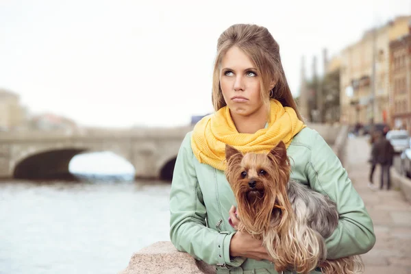 Sad young woman with small dog on the embarkment, waiting friend.