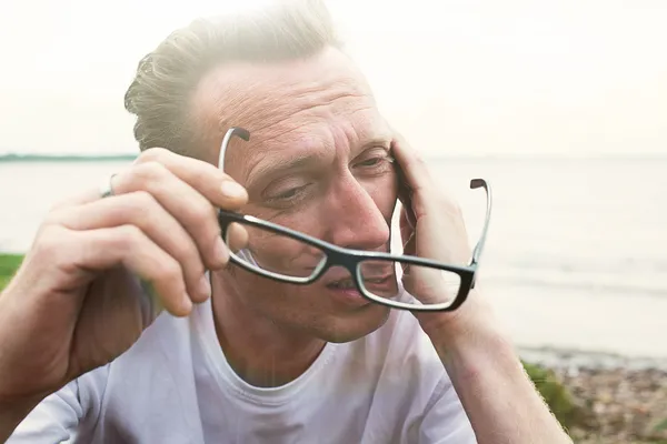 Man rub tired eyes on the beach after hard working day.