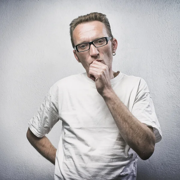 Thinking man on gray textured background. Portrait of a casual young pensive man looking into camera and gnaw nails.