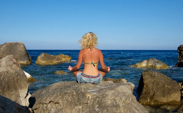 One woman sitting meditation on the stones with the view to the sea, woman meditation in wild nature, yoga with the view to the sea, wild nature and young woman siting on the coastline, relaxation