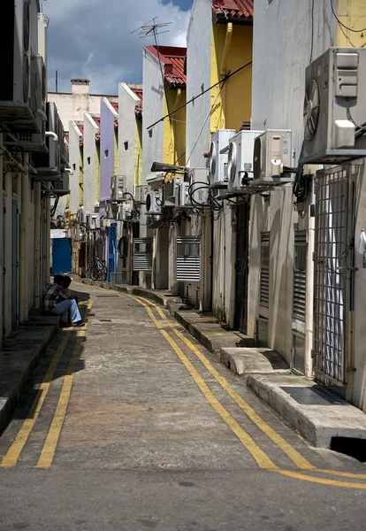 Narrow street with the shadows on sunny day in Singapore, Asia. Indian street. Narrow dirty street unknown man siting in background. Daily life in Singapore. Dirty typical asian street. Singapore.