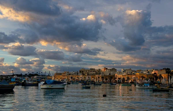 Malta Marsaxlokk village on dramatic sunset sky background, native fishing boats luzzus and ancient fishing village,fishing boats in golden sunset hours, evening light, landscape HDR photo