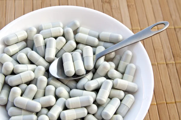 Capsules and pills on plate with spoon, close up