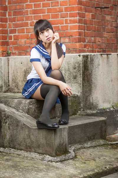 Asian schoolgirl sitting in front of school