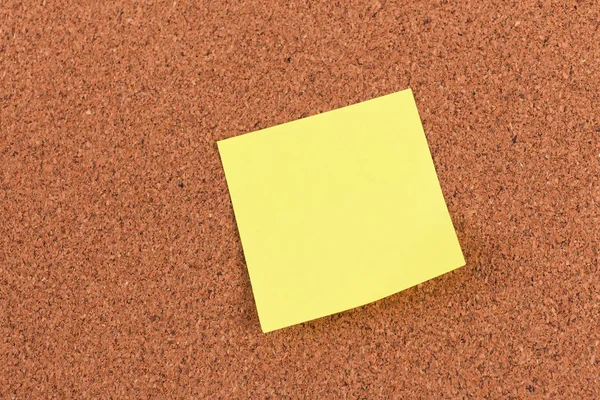 Yellow reminder sticky note on cork board, empty space for text