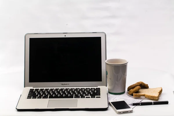 Laptop with cellphone , book bank, cookie, bread and cup of coff