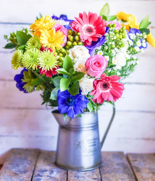 Colorful bouquet of spring flowers in vintage vase on rustic wooden background