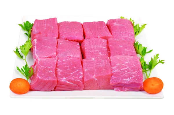 Raw fresh beef cubes on board with greens on white background