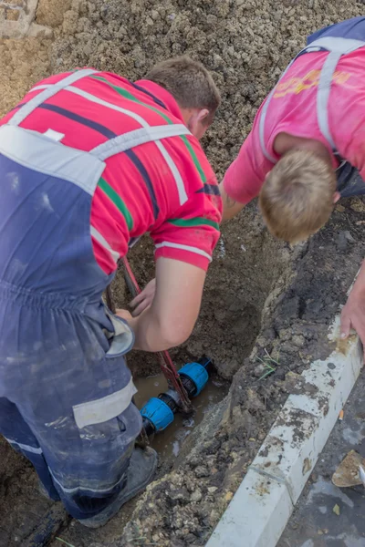 Utility workers holds wrench and in trench repair the broken pip