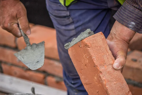 Builder worker with trowel building clay brick wall