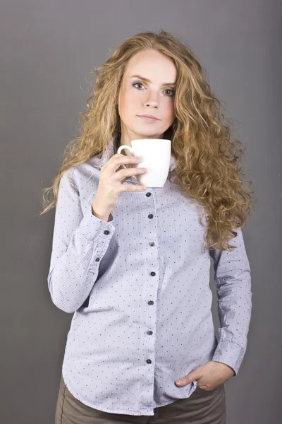 Lovely blonde with curly hair drinking tea or coffee from a white mug