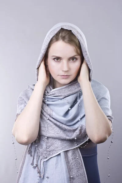 Lovely young blonde in a pale blue scarf on her head on gray background